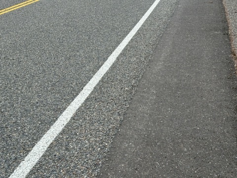 This photo shows the contrast between the chip seal on the left and smooth road on the right. 
